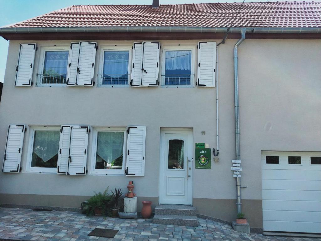 Casa blanca con ventanas blancas con persianas y puerta en Gîte LES PAPILLONS, en Bining-lès-Rohrbach