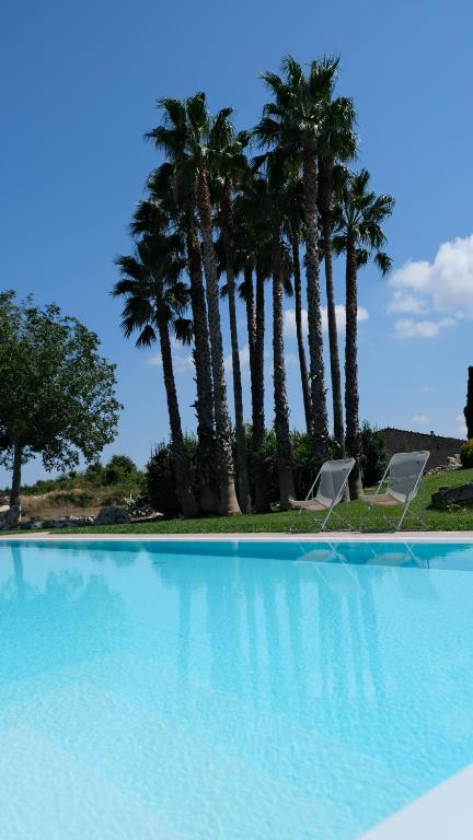 a swimming pool with two chairs and palm trees at Tenuta Aguglia in Noto