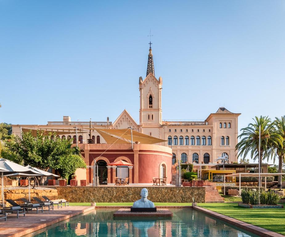 a building with a fountain in front of a building with a church at Sant Pere del Bosc Hotel & Spa - Adults Only in Lloret de Mar