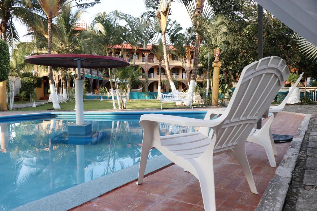 two chairs and an umbrella next to a swimming pool at Hotel HF Hacienda San Francisco in Puente Nacional