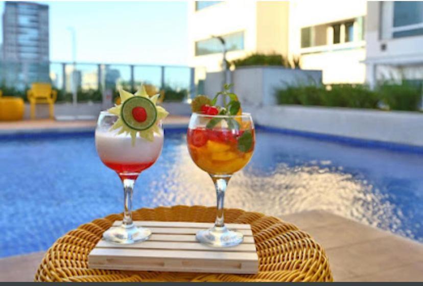 two glasses of drinks on a table next to a pool at Flat no Transamerica Hotel in Campos dos Goytacazes