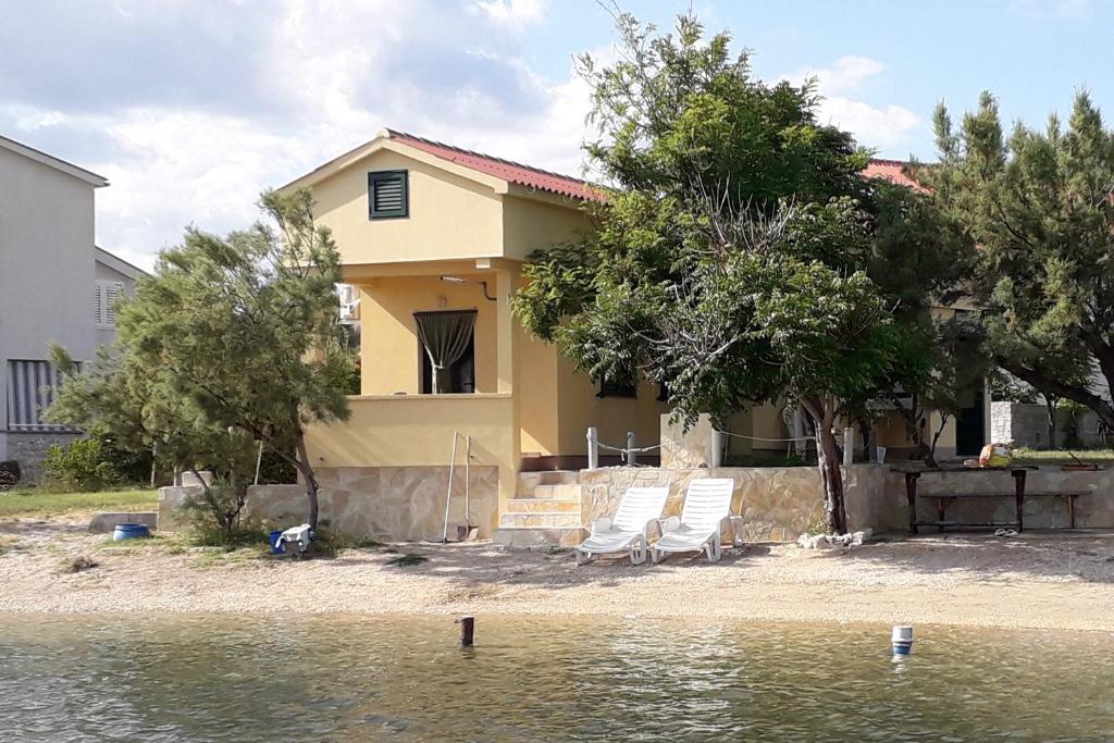 a house with two lawn chairs and some water at Apartments by the sea Dinjiska, Pag - 9386 in Povljana