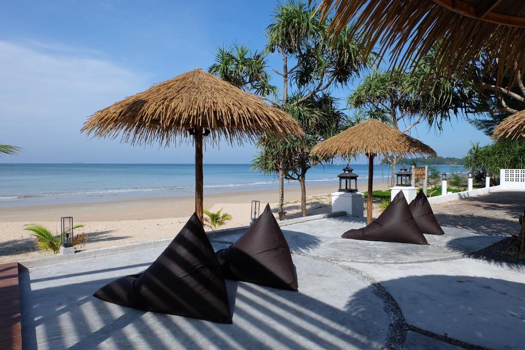 a table with pillows and straw umbrellas on a beach at Lanta Sea House in Ko Lanta