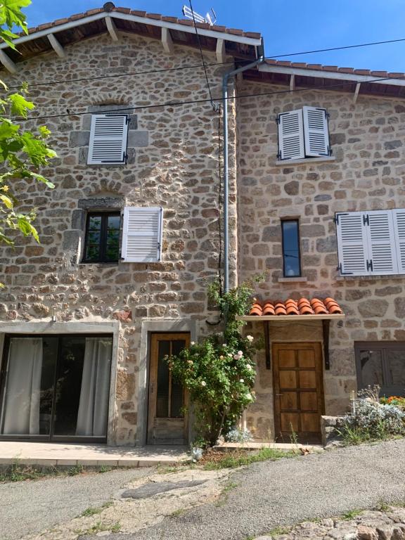 uma grande casa de pedra com persianas brancas em Gîte Le doux Valoan em Lamastre