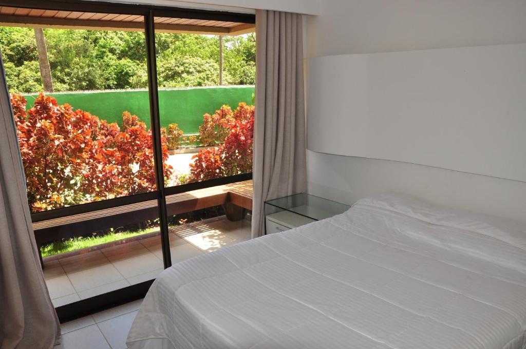 a bedroom with a bed and a large window at Nannai Residence Apartament in Porto De Galinhas