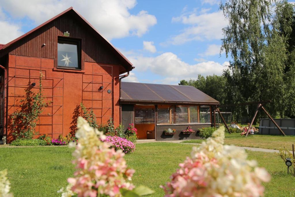 a red barn with a window and flowers in the yard at Viesu māja Ramatas in Skulte