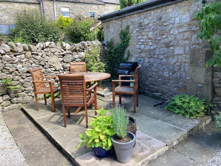 a patio with a table and chairs and a stone wall at Bluebell Cottage in the Yorkshire Dales in Stainforth