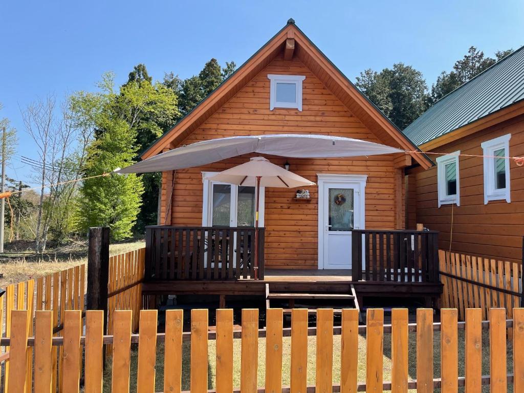 ein Holzhaus mit einer Veranda mit einem Sonnenschirm in der Unterkunft Biwako Hills Resort - Vacation STAY 99556v in Takashima