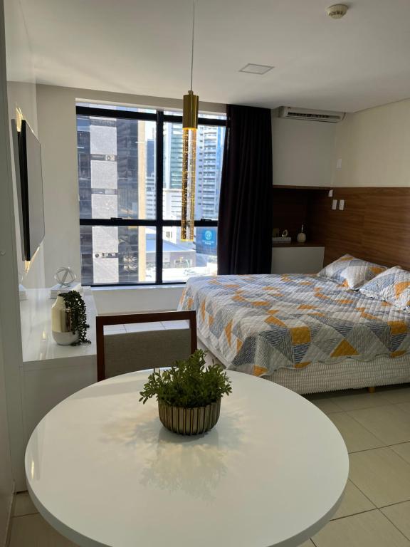 een slaapkamer met een bed en een witte tafel met een potplant bij Suíte luxo com tela de cinema no América Towers Studio Residence in Salvador