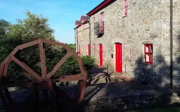 a stone building with red windows and a wooden gate at The Old Mill, Kilcorkey, Bellanagare, Castlerea, County Roscommon - West of Ireland in Bellanagare