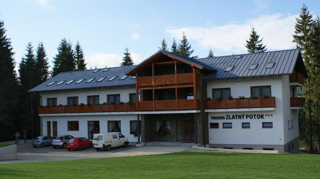 un gran edificio con coches estacionados en un estacionamiento en Penzión Zlatny Potok en Mutné