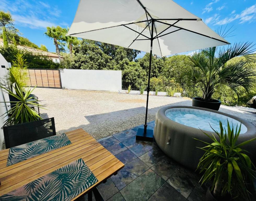 uma banheira de hidromassagem com um guarda-sol no pátio em Villa Les Oliviers Spa privatif em Bandol