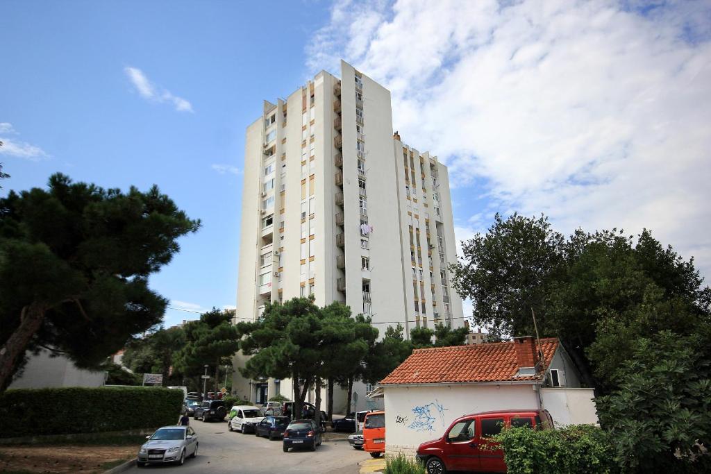 a tall white building with cars parked in a parking lot at Holiday apartments Split - 10315 in Split