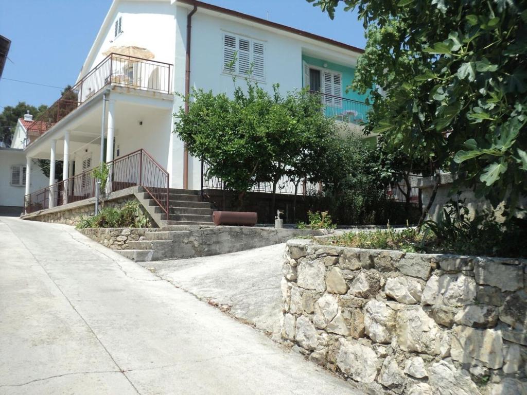 a white house with a stone wall next to a street at Rooms by the sea Banjol, Rab - 11716 in Rab