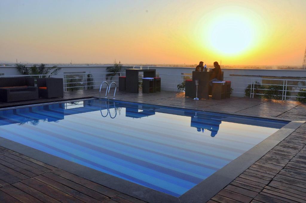 a swimming pool on the roof of a building with a sunset at Hotel Marigold Jaipur in Jaipur