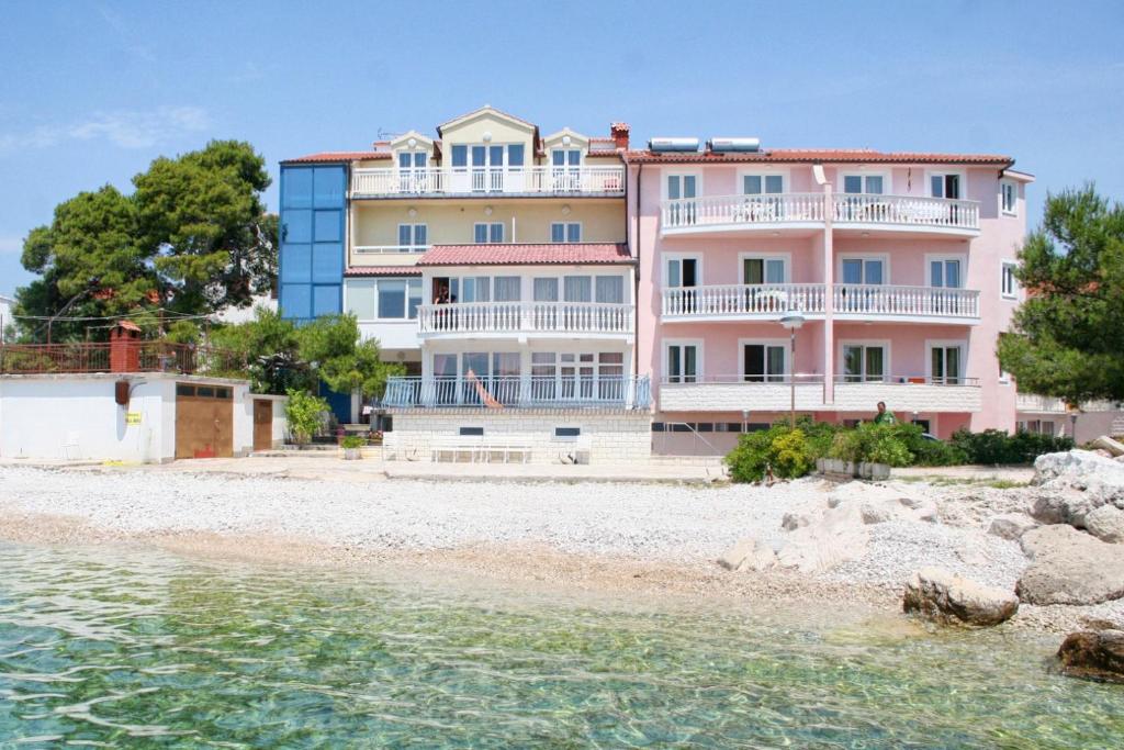 ein rosafarbenes Gebäude am Strand mit dem Wasser in der Unterkunft Apartments by the sea Primosten - 9687 in Primošten