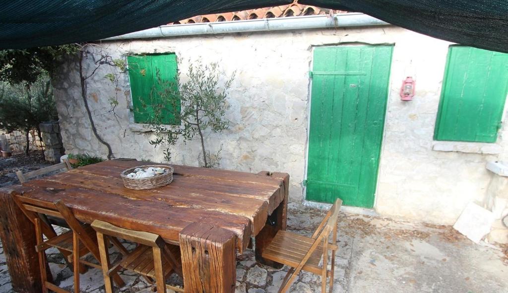 une table et des chaises en bois devant un bâtiment avec des portes vertes dans l'établissement Secluded fisherman's cottage Radelj, Murter - 12155, à Murter