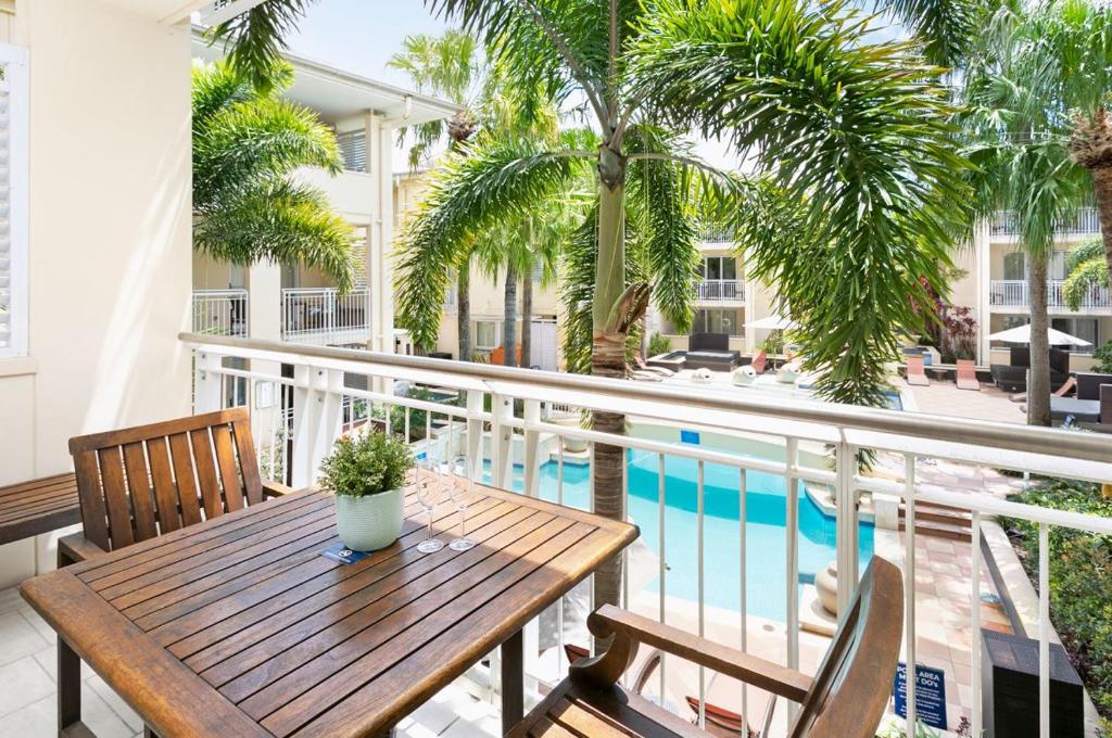 a balcony with a wooden table and chairs and a swimming pool at Laguna on Hastings Noosa 127 in Noosa Heads