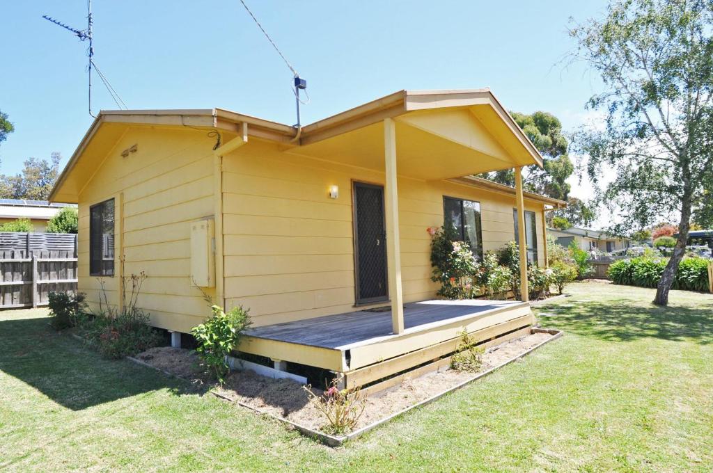 a yellow house with a porch in a yard at Alwyns By The Sea in Inverloch