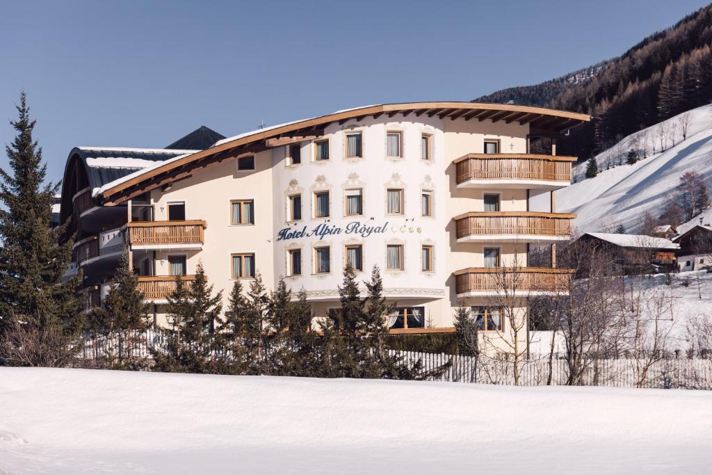 Un grand bâtiment blanc avec des balcons en bois dans la neige dans l'établissement Wellness Refugium & Resort Hotel Alpin Royal - Small Luxury Hotels of the World, à Cadipietra