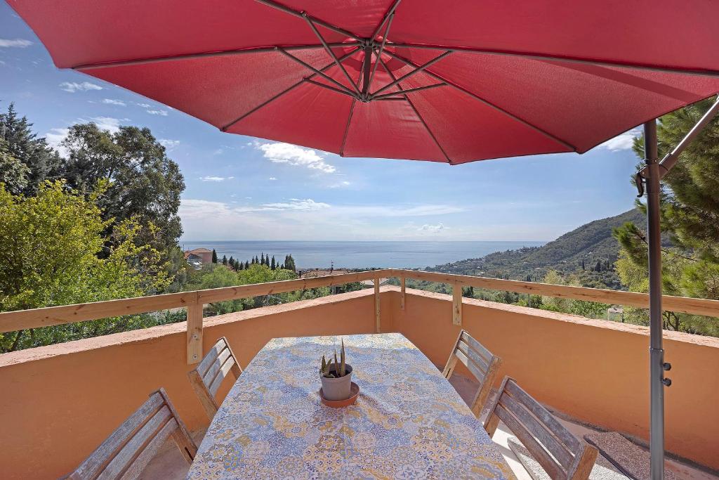 una mesa con una sombrilla roja en el balcón en La Colombera, en Alassio
