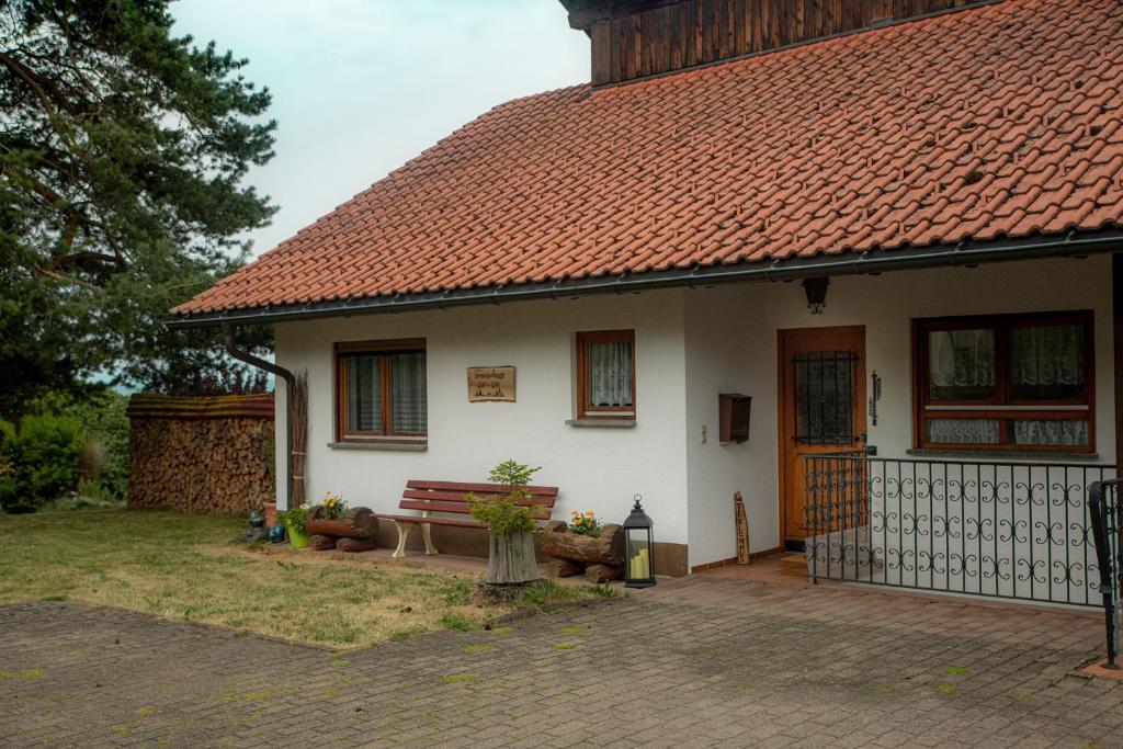 ein weißes Haus mit einem roten Dach und einer Bank in der Unterkunft Ferienwohnung Wald & Wild in Löffingen