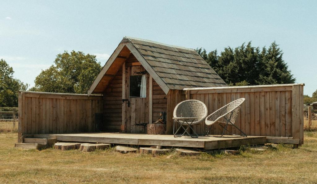un petit hangar en bois avec deux chaises dans un champ dans l'établissement Glamping at the Retreat Wiltshire is rural bliss, à Chippenham