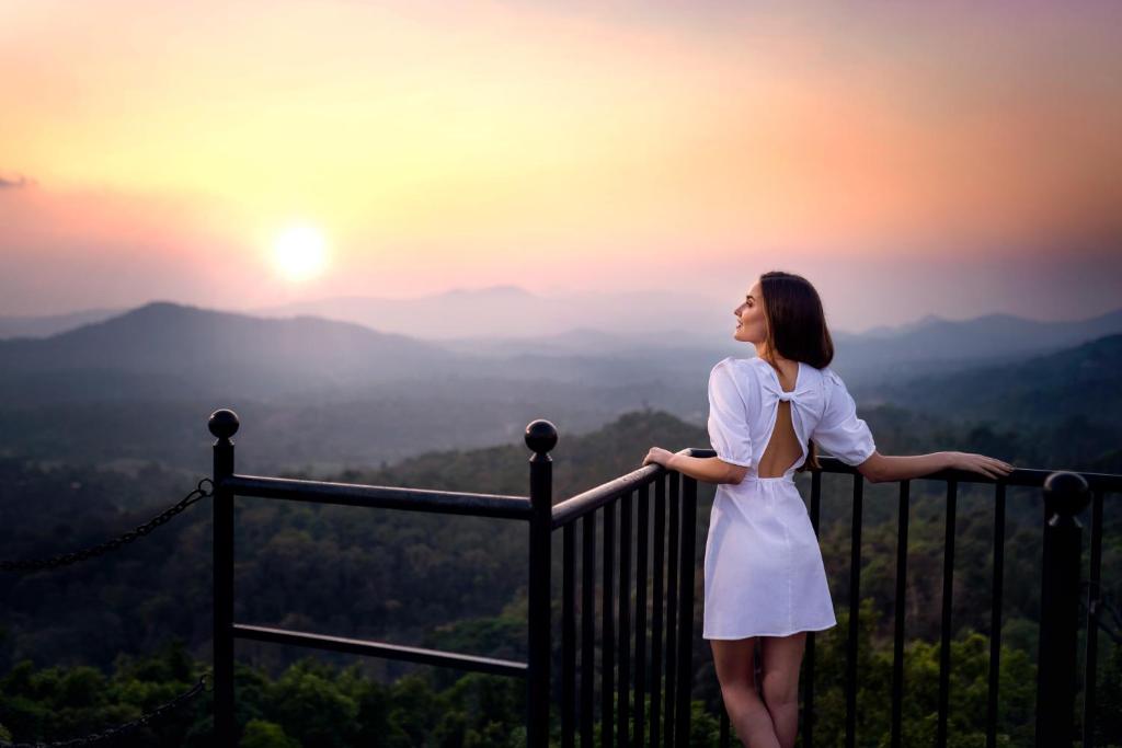 una mujer parada en un balcón con vistas a la puesta de sol en Coorg Wilderness Resort & Spa, en Madikeri