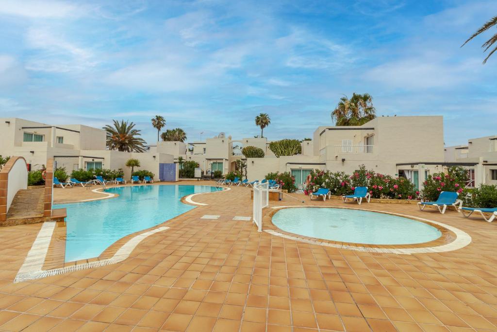 a swimming pool in a resort with chairs and trees at Flatguest Alisios Playa 4 in Corralejo
