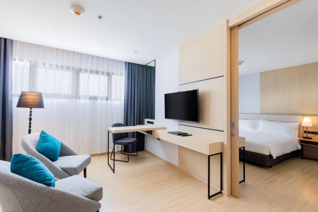 A room with a large desk, television, two lounge chairs and a mirrored bedroom partition.