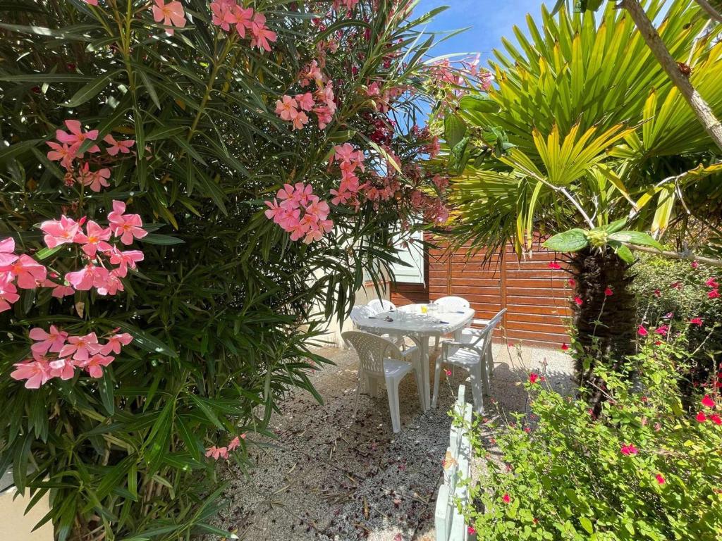 une table et des chaises dans un jardin avec des fleurs roses dans l'établissement Charmante maison avec jardin, parking, piscines chauffées à 2 pas de l'océan - St Jean de Monts - FR-1-224C-46, à Saint-Jean-de-Monts