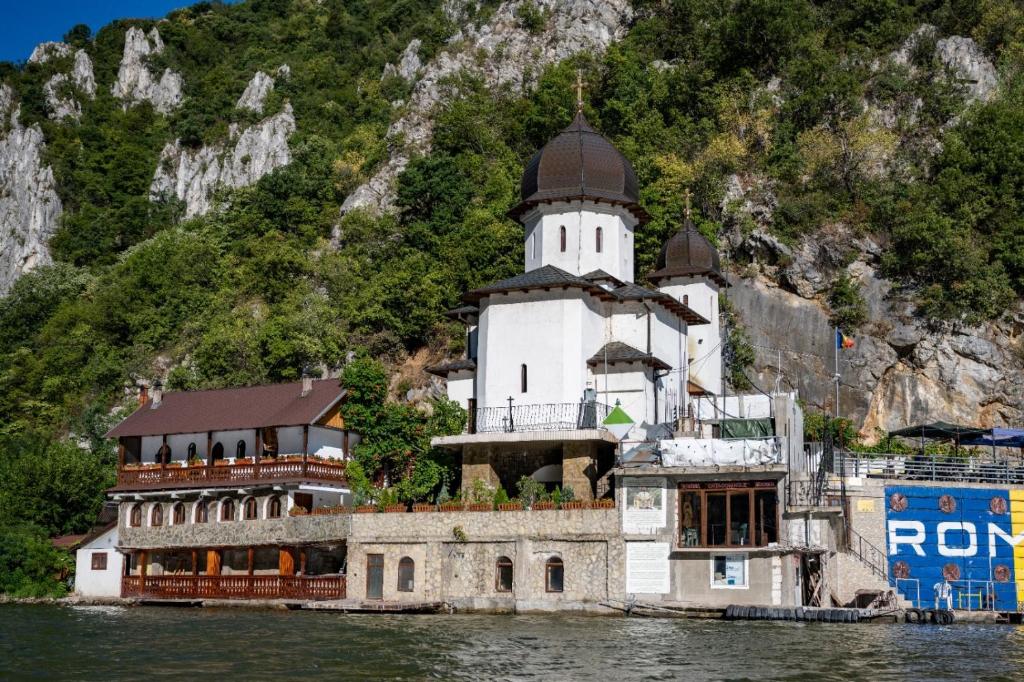 a building on the water in front of a mountain at Casa Clau Cazare Orșova in Orşova