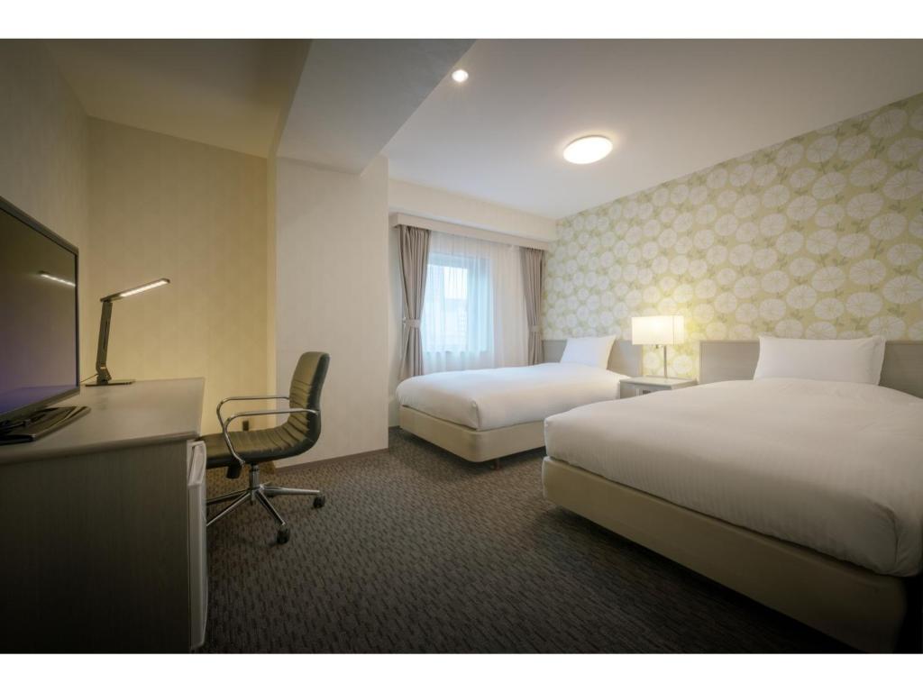 a hotel room with two beds and a desk and a television at Hotel Ronshan Sapporo - Vacation STAY 64963v in Sapporo