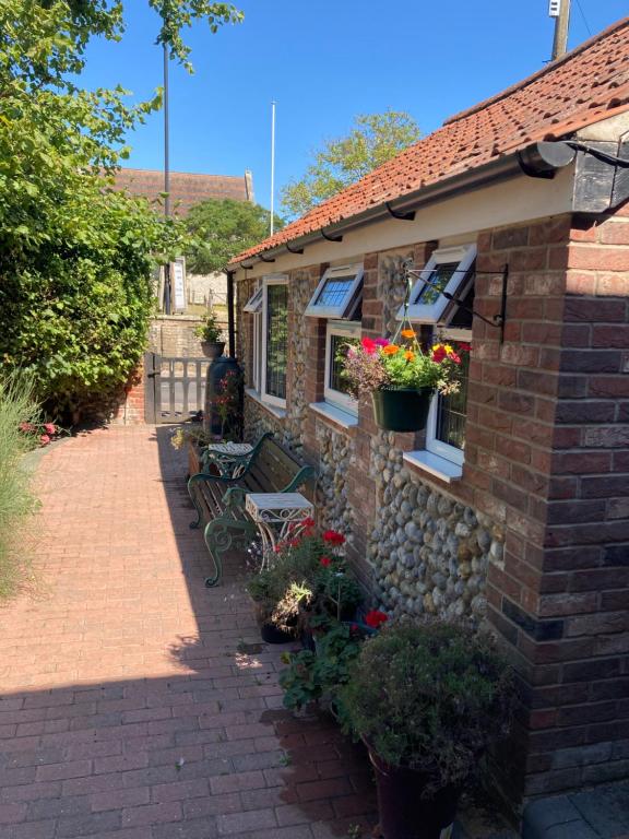 une maison en briques avec un banc et des fleurs sur elle dans l'établissement The Old Barn Annexe, à West Runton