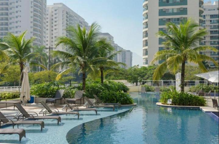 une piscine avec des chaises et des palmiers dans une ville dans l'établissement Suíte Verano Stay Barra, à Rio de Janeiro