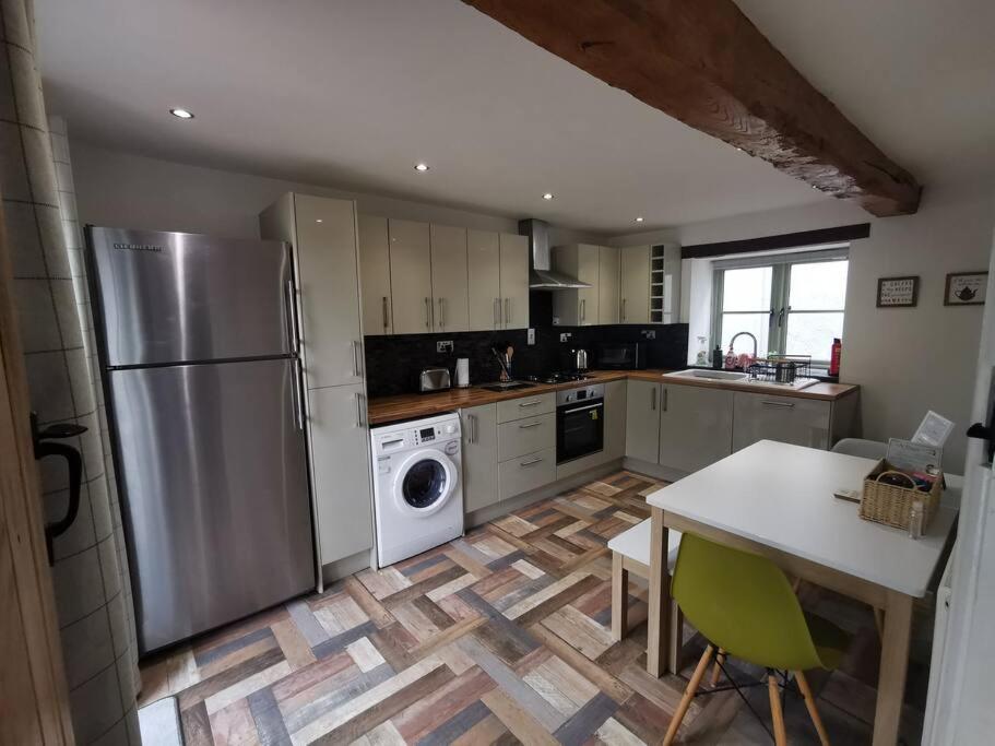 uma cozinha com um frigorífico de aço inoxidável e uma mesa em Lovely two bedroom cottage with private garden em Kingswood