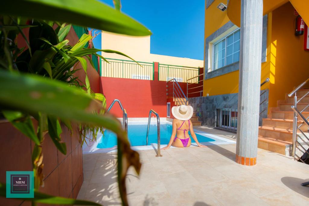 a woman in a hat standing next to a swimming pool at Inma Apartment Montaña La Data in San Bartolomé de Tirajana