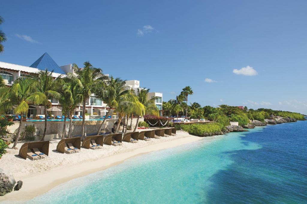 una playa con sillas y palmeras junto al agua en Zoetry Villa Rolandi Isla Mujeres Cancun - All Inclusive, en Isla Mujeres