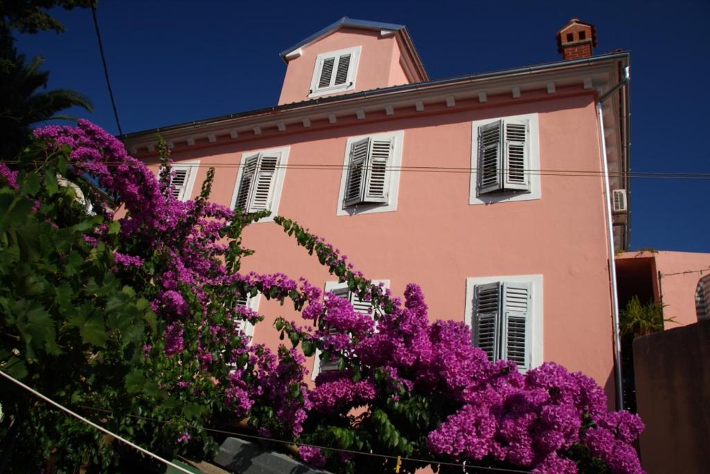 a pink building with windows and purple flowers at Apartment Mali Losinj 12634a in Veli Lošinj