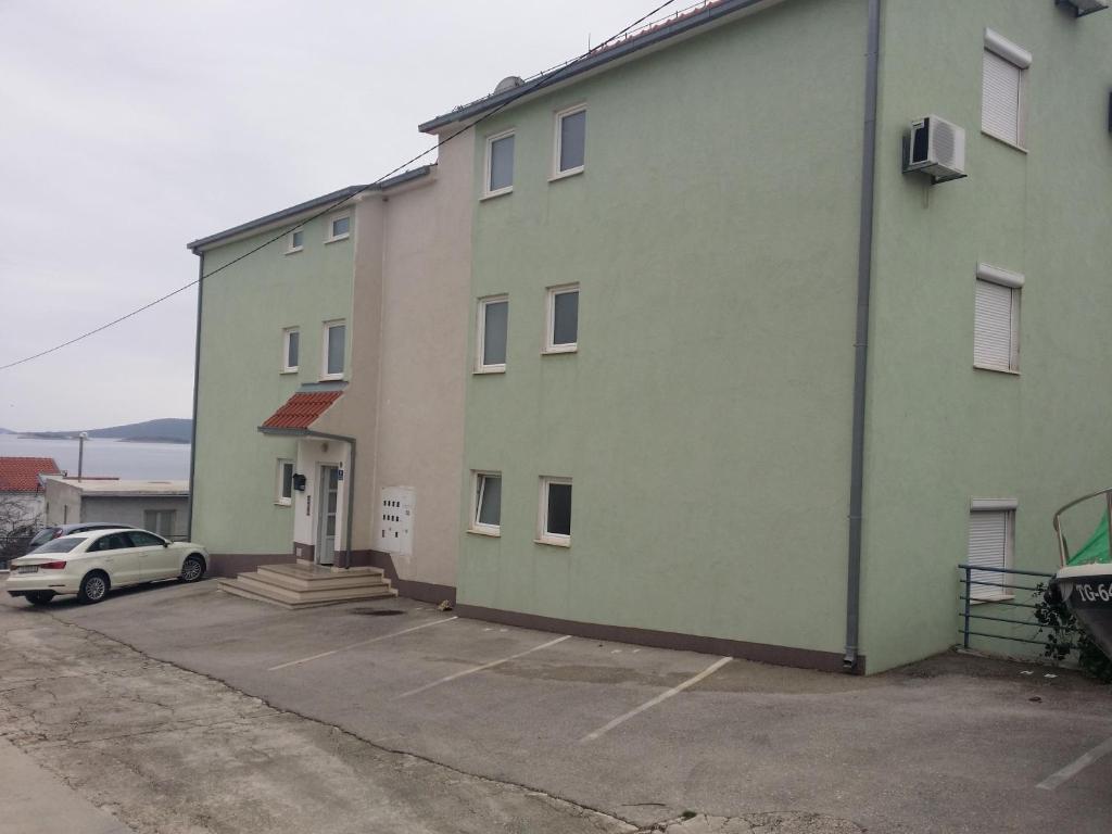 a green building with a car parked in a parking lot at Apartments by the sea Seget Vranjica, Trogir - 12915 in Trogir