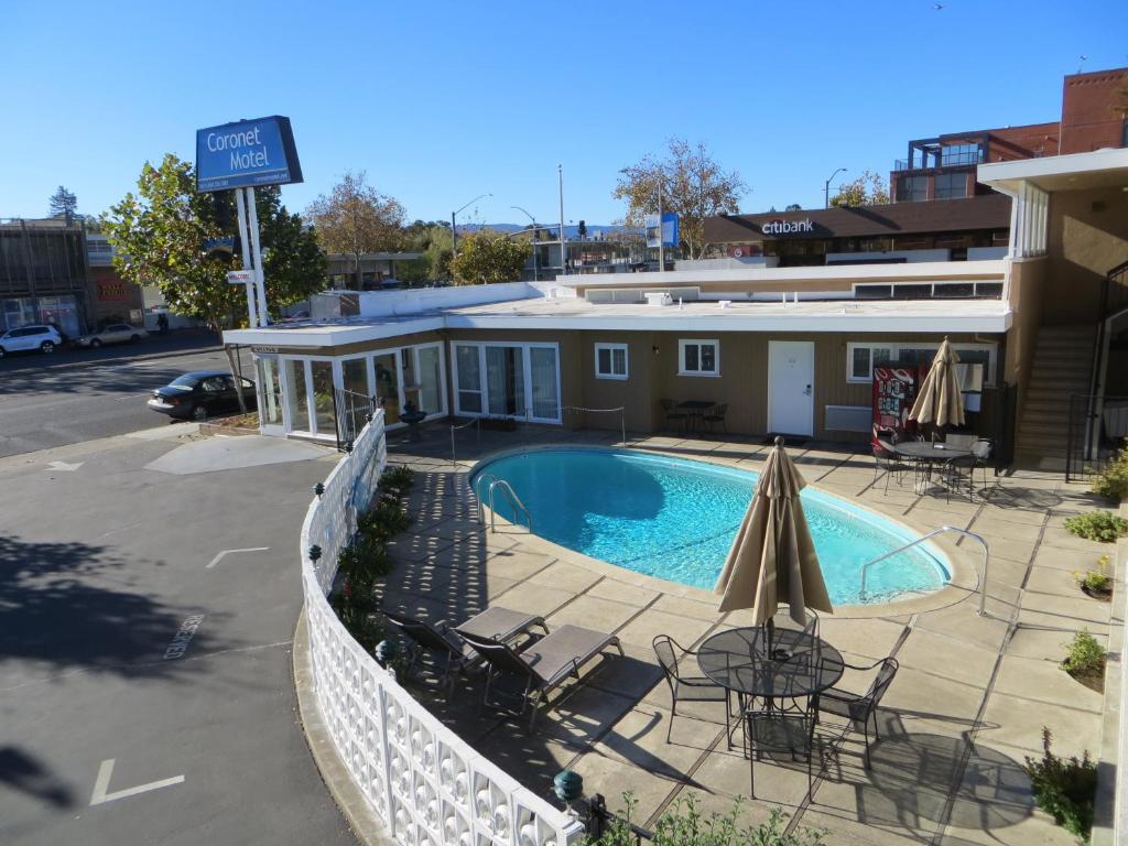 una piscina con sillas y una sombrilla junto a un edificio en Coronet Motel, en Palo Alto