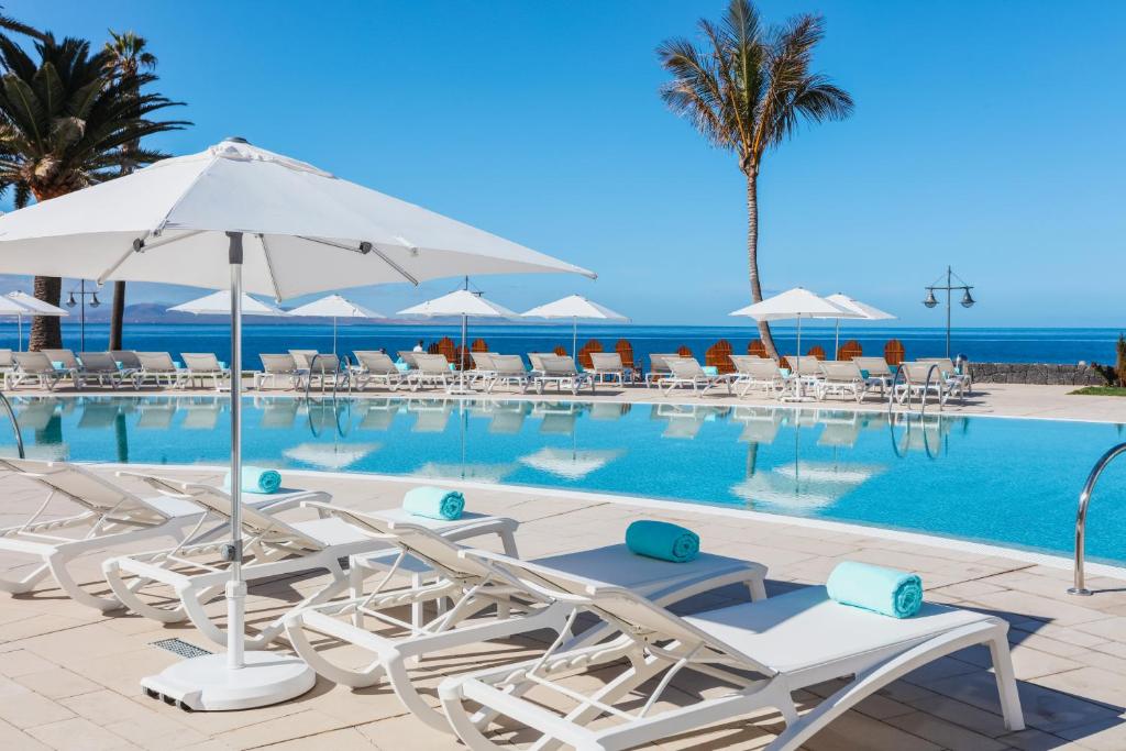 een zwembad met stoelen en parasols en de oceaan bij Iberostar Selection Lanzarote Park in Playa Blanca