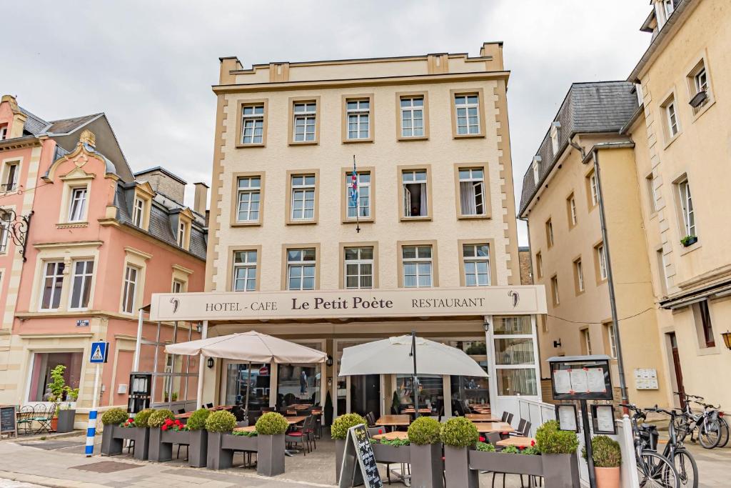 ein Gebäude mit Tischen und Sonnenschirmen davor in der Unterkunft Hôtel Le Petit Poète in Echternach