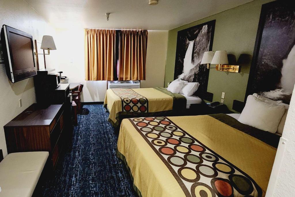 a hotel room with three beds and a flat screen tv at Super 8 by Wyndham Rawlins Wyoming in Rawlins