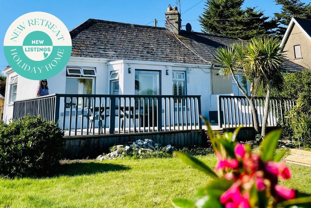 a white house with a fence and flowers in front of it at Wavecrest Holiday Cottage in Garryvoe