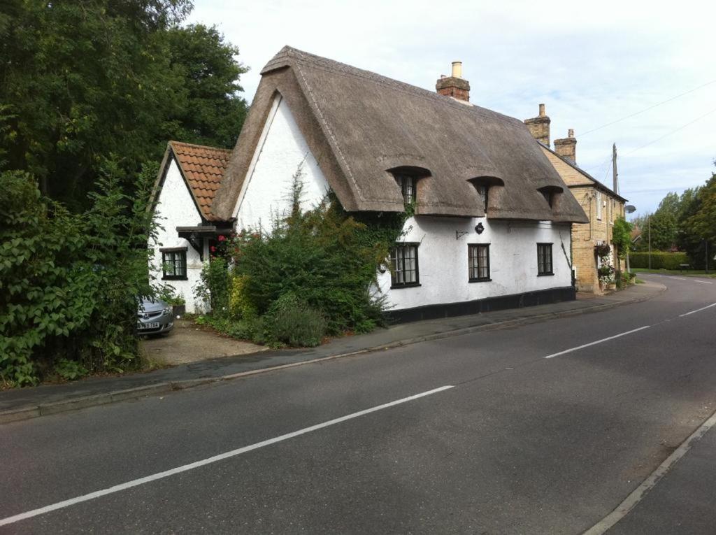 a white house with a roof on the side of a road at Quirky 18th Century Thatched Cottage in Great Staughton