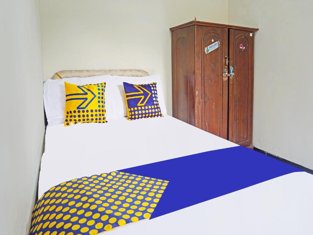 een bed met gele en blauwe kussens en een houten kast bij OYO LIFE 91551 Gwen Syariah Homestay in Malang