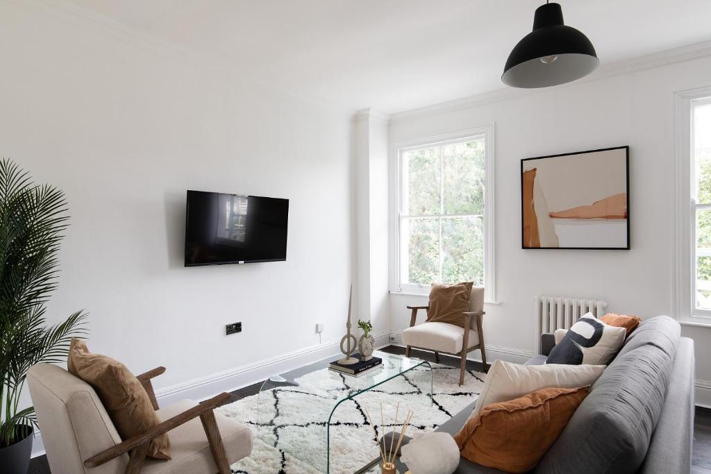 The Camberwell Retreat - Alluring 2BDR Flat with Garden في لندن: غرفة معيشة مع أريكة وتلفزيون على الحائط