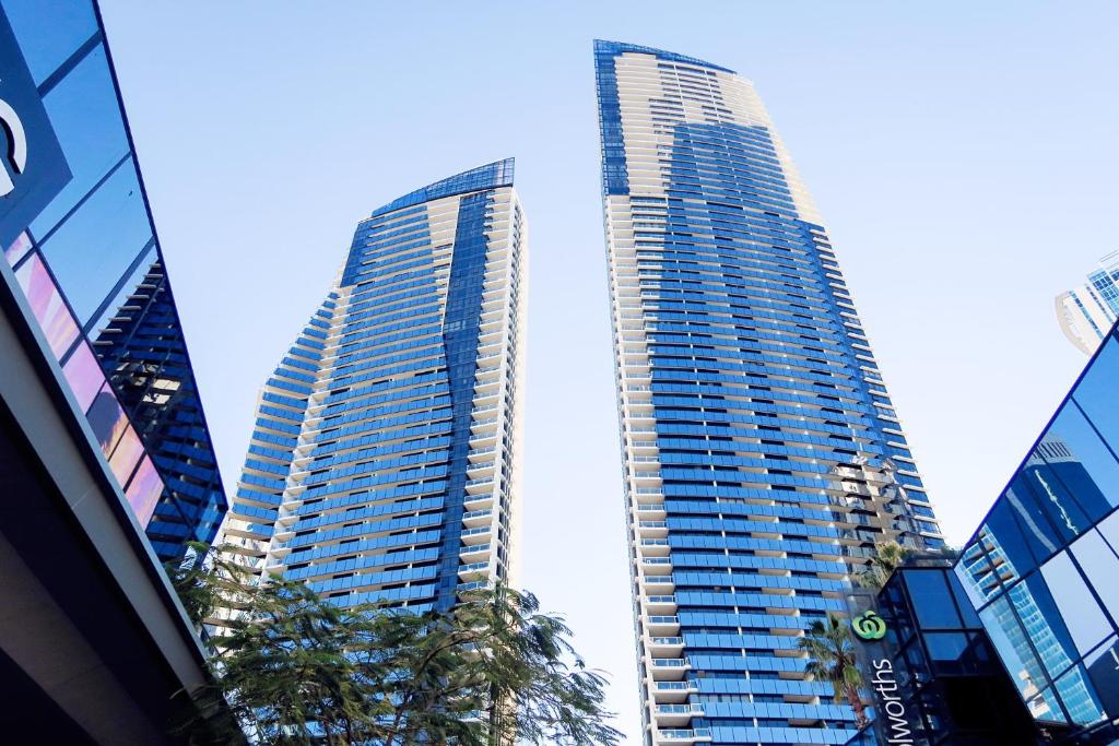 two tall buildings in a city with palm trees at Circle On Cavill Surfers Paradise Apartments-Holiday Paradise in Gold Coast