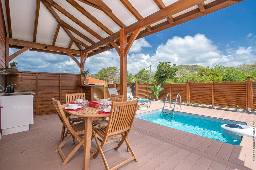 un patio con mesa, sillas y piscina en Bungalow Pom 1, piscine, à 5 min des plages en Le Vauclin